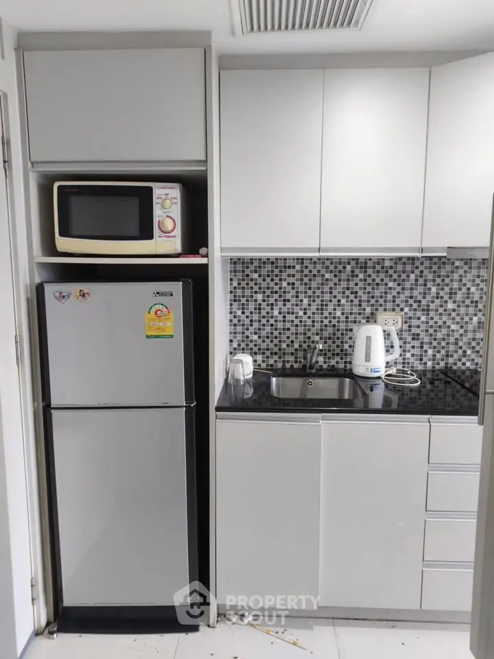 Modern compact kitchen with sleek cabinets, microwave, fridge, and stylish backsplash.