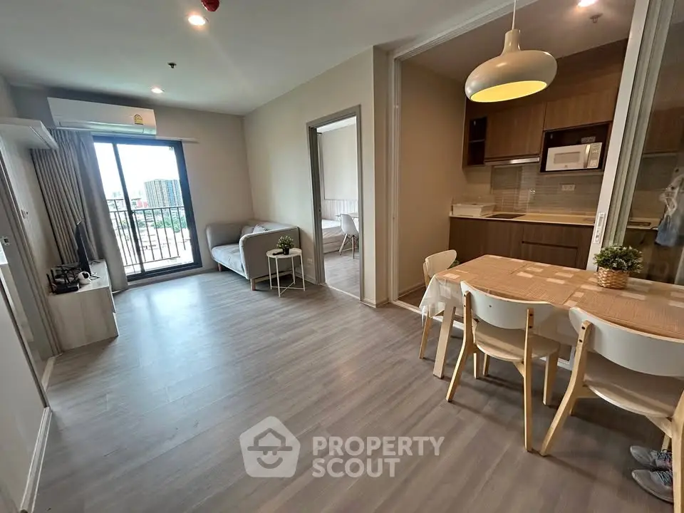 Modern open-plan living room with dining area and kitchen, featuring sleek flooring and balcony access.
