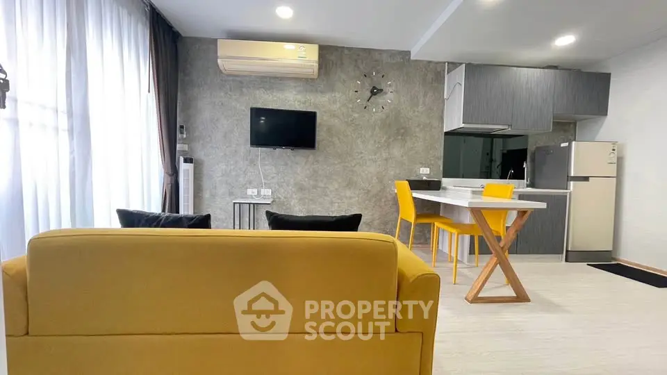 Modern open-plan living room with stylish kitchen and vibrant yellow sofa.