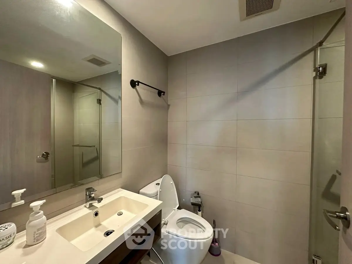 Modern bathroom with sleek fixtures and glass shower enclosure in contemporary apartment.