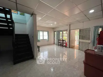 Spacious living area with tiled flooring and ample natural light, featuring a staircase and open layout.