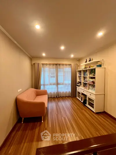 Cozy living room with wooden flooring and elegant lighting, featuring a stylish sofa and modern shelving unit.