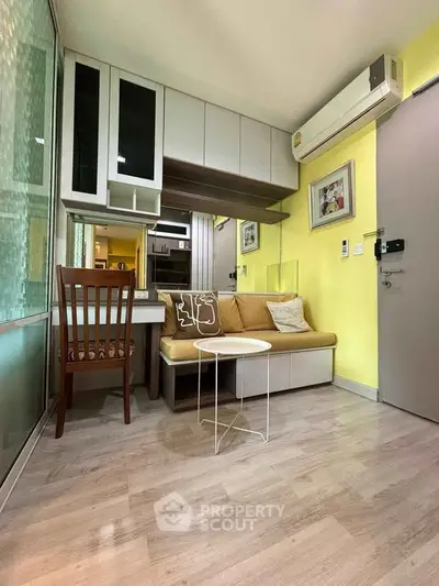 Cozy living room with modern decor, featuring a compact sofa, wooden chair, and wall-mounted air conditioner.
