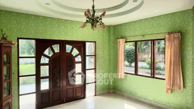 Charming living room with elegant wooden door and lush garden view, featuring classic chandelier and vibrant green walls.