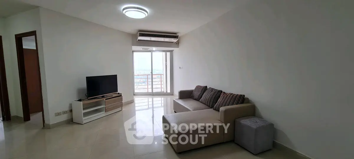 Spacious living room with modern sofa and TV, featuring a bright balcony view.