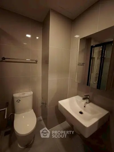 Modern bathroom with sleek fixtures and neutral tiles, featuring a wall-mounted sink and toilet.