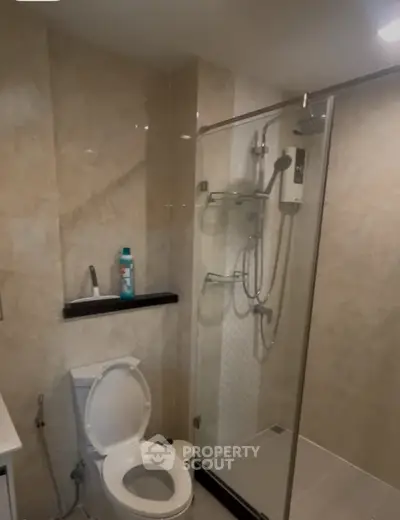 Modern bathroom with glass shower and beige tiles, featuring a sleek design.
