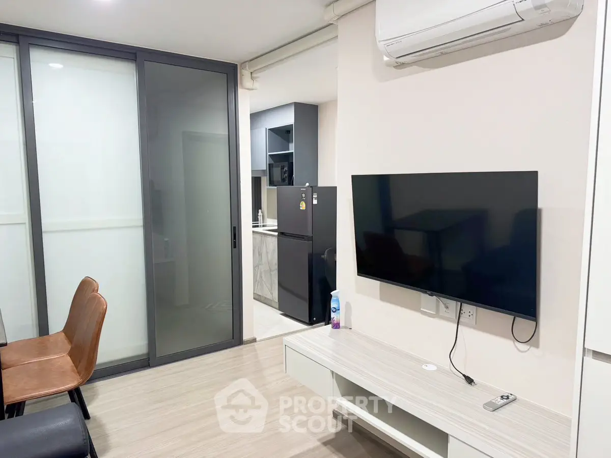 Modern living room with sleek design, featuring a wall-mounted TV and air conditioning, adjacent to a compact kitchen.