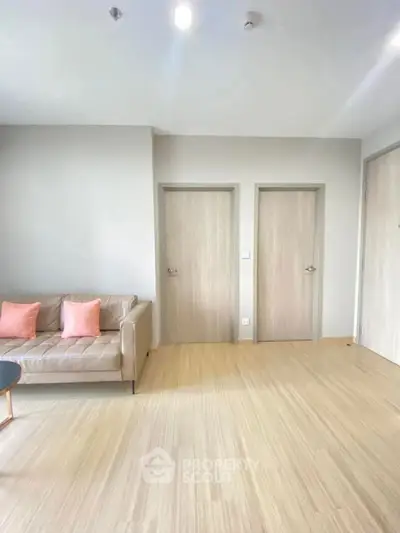 Modern living room with beige sofa and wooden flooring, featuring minimalistic design.