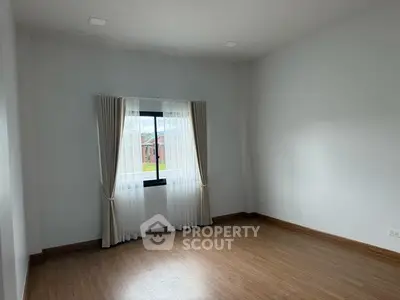 Spacious empty room with wooden flooring and large window with curtains
