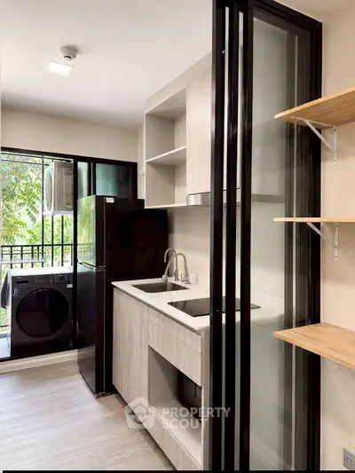 Modern kitchen with sleek design, featuring a black fridge, washing machine, and sliding glass doors.