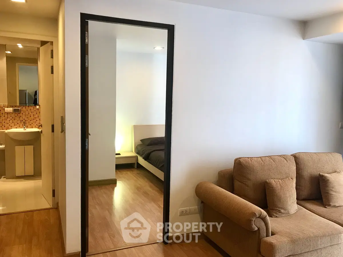 Modern apartment interior with cozy living room and bedroom view, featuring wooden flooring and neutral decor.
