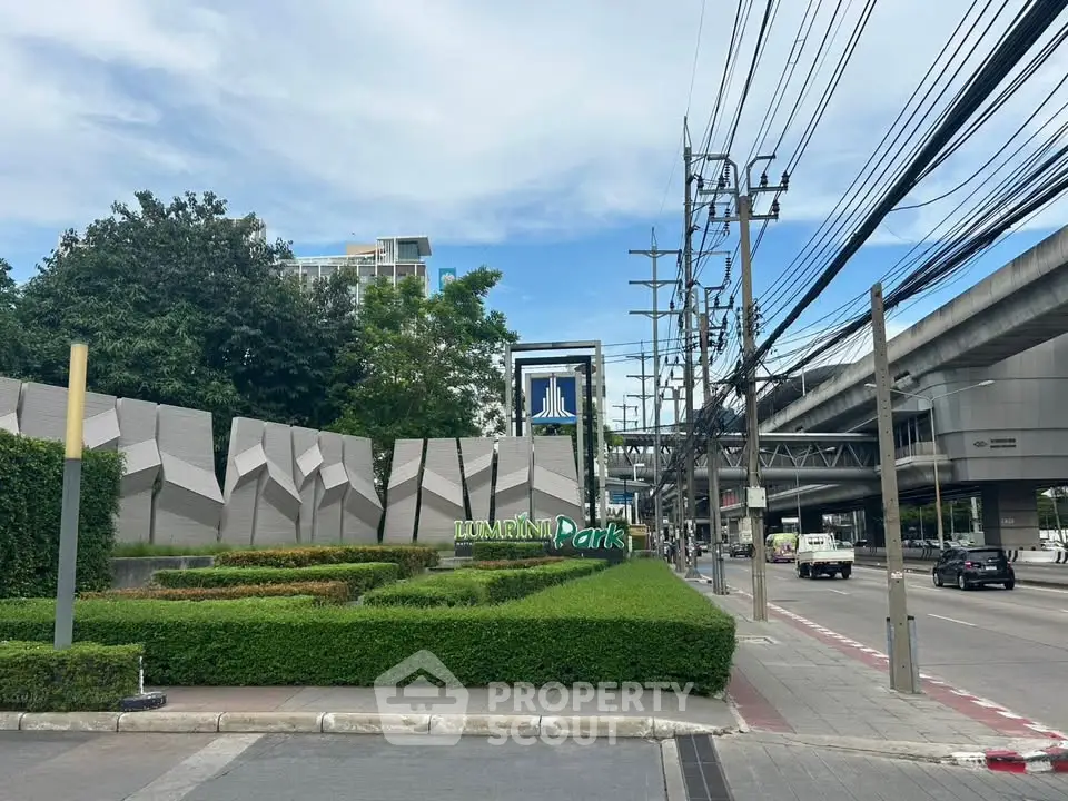 Modern urban park entrance with lush greenery and contemporary design near city infrastructure.