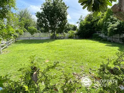 Spacious green garden with lush trees and fenced boundary, perfect for outdoor activities.