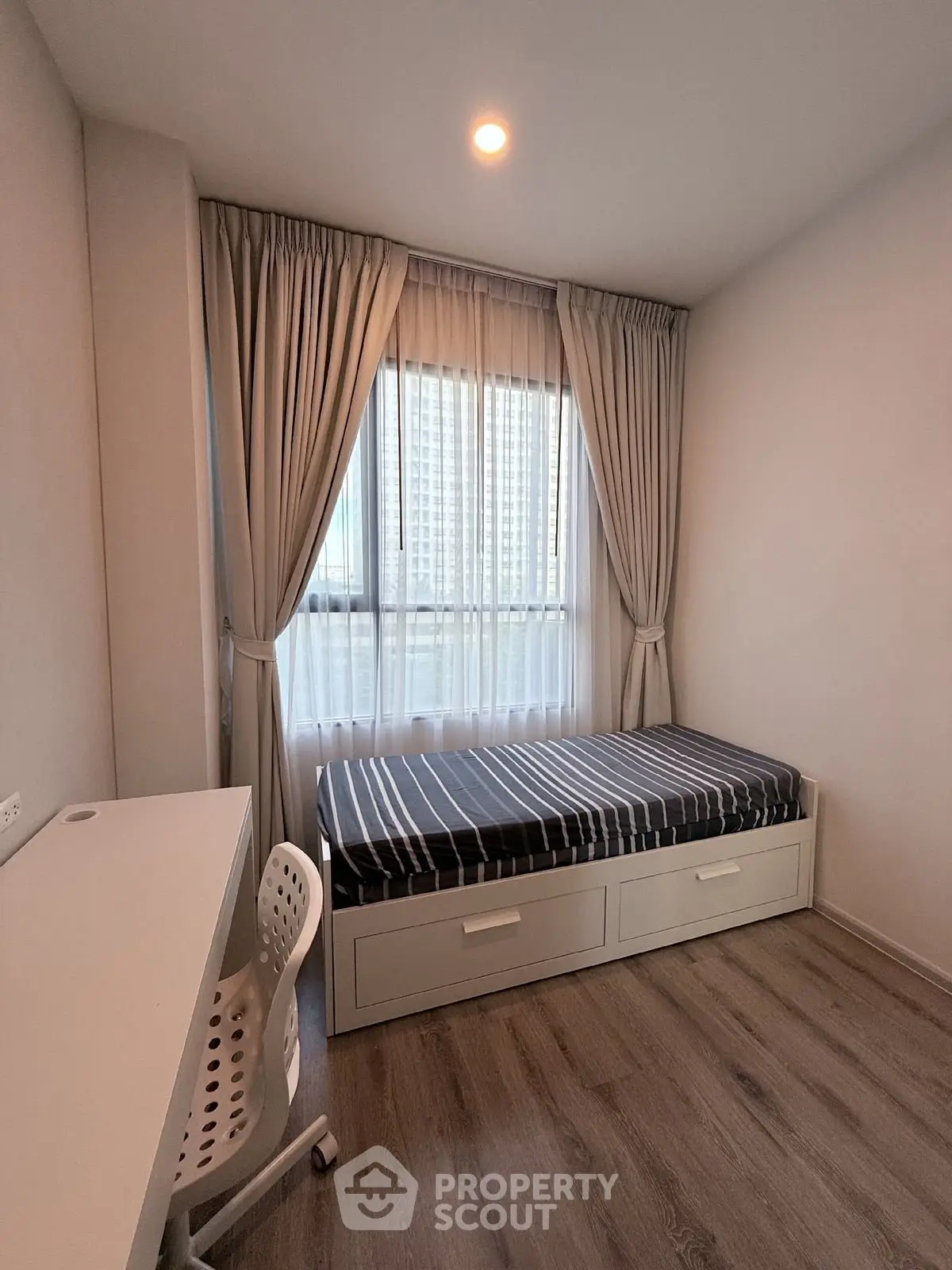 Cozy bedroom with single bed, study desk, and large window with city view.