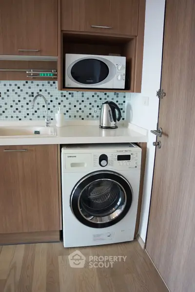 Modern kitchen with built-in appliances including washing machine and microwave, sleek wooden cabinets.