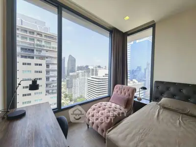 Modern bedroom with stunning city view, featuring a stylish chaise lounge and sleek workspace.
