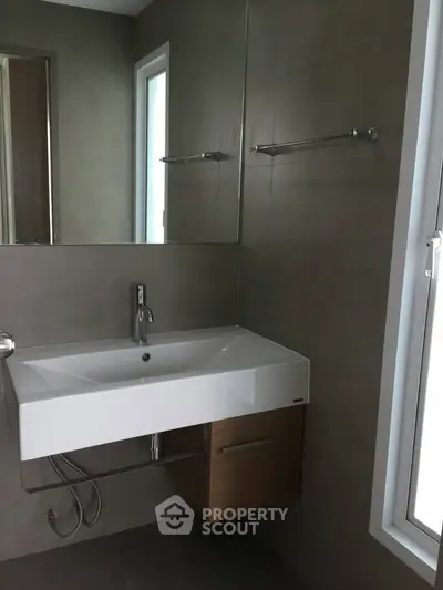 Modern bathroom with sleek sink and large mirror, featuring contemporary design and natural light.