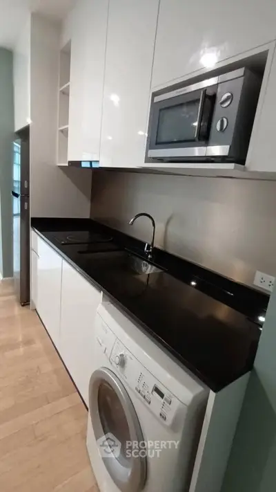 Modern kitchen with sleek black countertop, built-in microwave, and washing machine in compact layout.