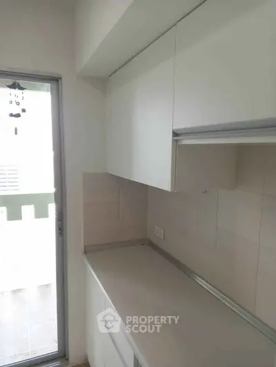 Modern kitchen with sleek white cabinets and natural light from glass door.