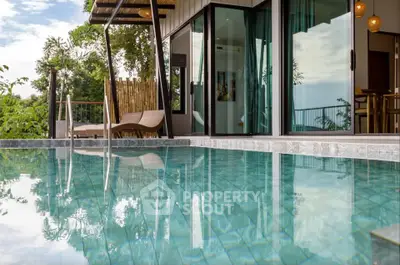 Luxurious poolside view of modern villa with open glass doors and lush greenery.