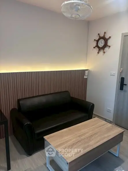Modern living room with black leather sofa and wooden coffee table, featuring nautical wall decor.