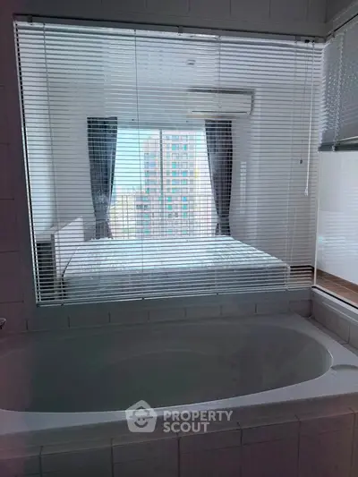 Modern apartment with a unique bathroom view into a bright bedroom, featuring a bathtub and large windows.