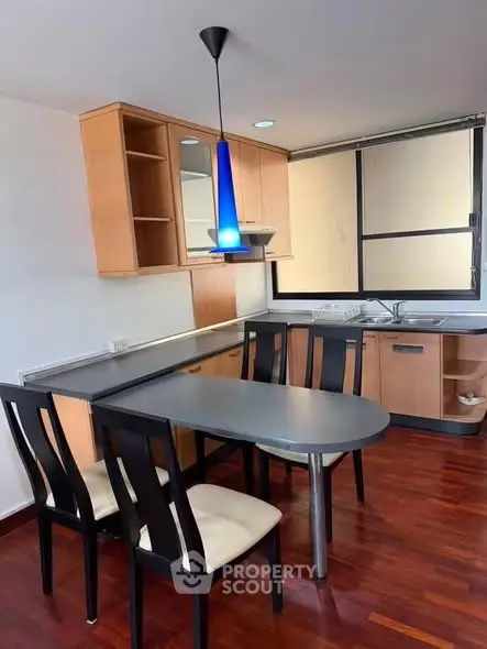 Modern kitchen with sleek design, featuring wooden cabinets, black dining table, and blue pendant light.