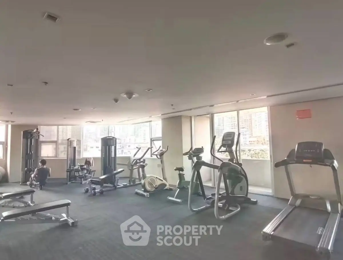Spacious gym with modern equipment and city view in luxury apartment building.