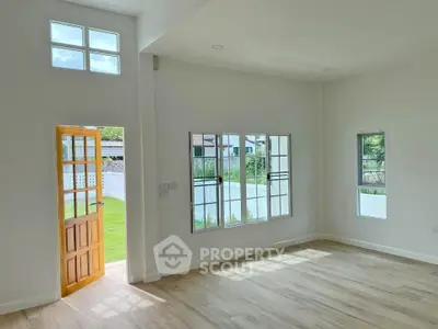 Bright and spacious living room with large windows and wooden door opening to a lush garden view.