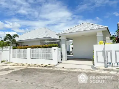 Modern white house with tiled roof and gated entrance under clear blue sky