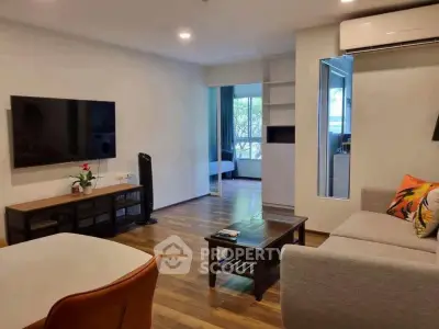 Modern living room with sleek furniture and large TV, featuring a glimpse into a cozy bedroom.
