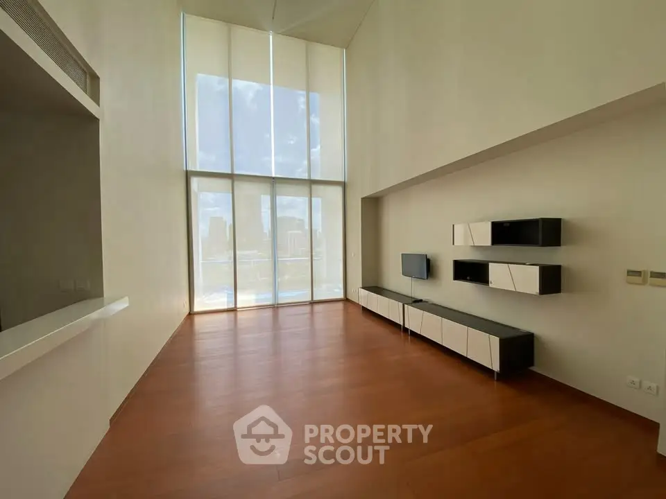 Spacious modern living room with high ceilings and large windows offering city views.