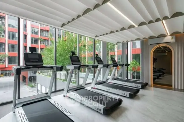 Modern gym with multiple treadmills and large windows overlooking urban scenery.