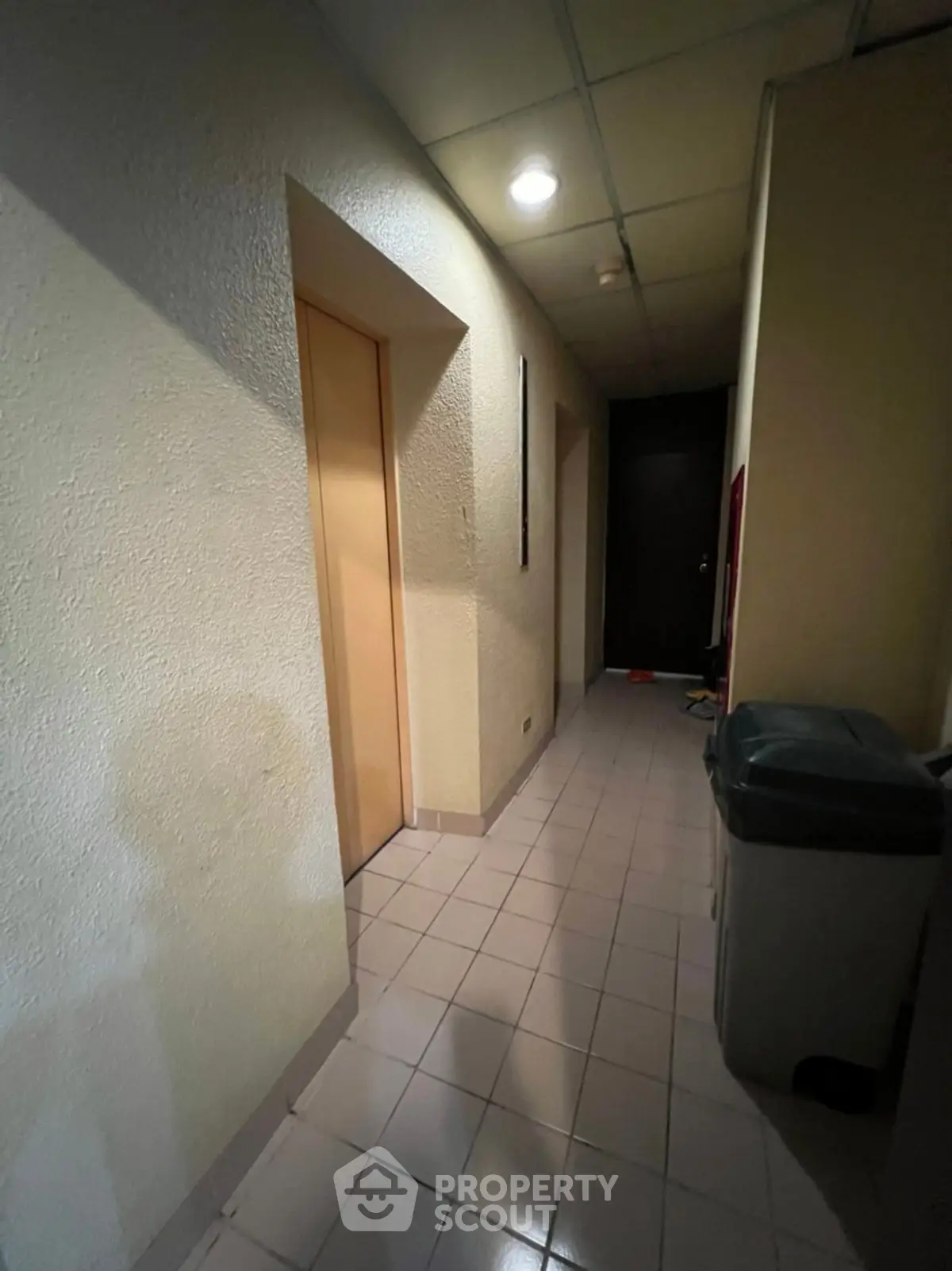 Dimly lit hallway with tiled floor and elevator access, ideal for residential or commercial properties.