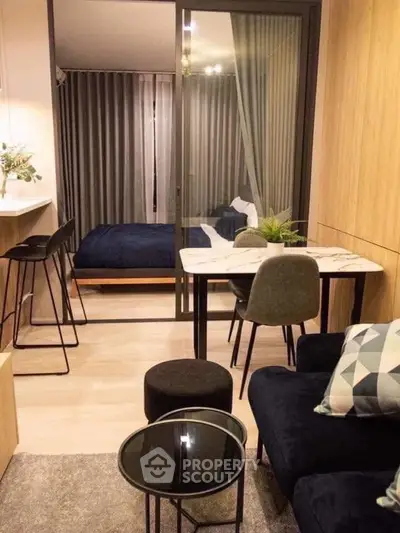 Modern studio apartment with cozy living area and stylish bedroom separated by glass partition.