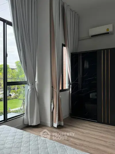 Modern bedroom with large windows and elegant curtains, featuring a sleek black wardrobe and air conditioning.