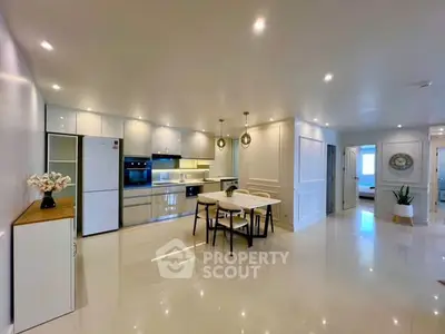 Spacious modern kitchen with sleek white cabinetry and dining area in open layout apartment.