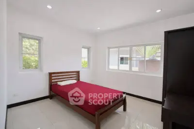 Bright minimalist bedroom with red bedspread and large windows offering natural light.