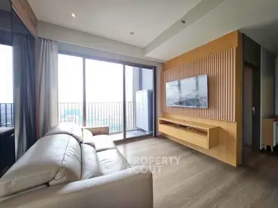Modern living room with large windows and balcony access, featuring sleek furniture and wooden accents.
