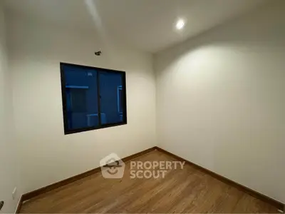 Spacious empty room with wooden flooring and a large window, perfect for customization.