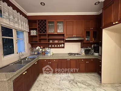 Spacious kitchen with wooden cabinets and marble flooring, featuring a gas stove and ample storage.