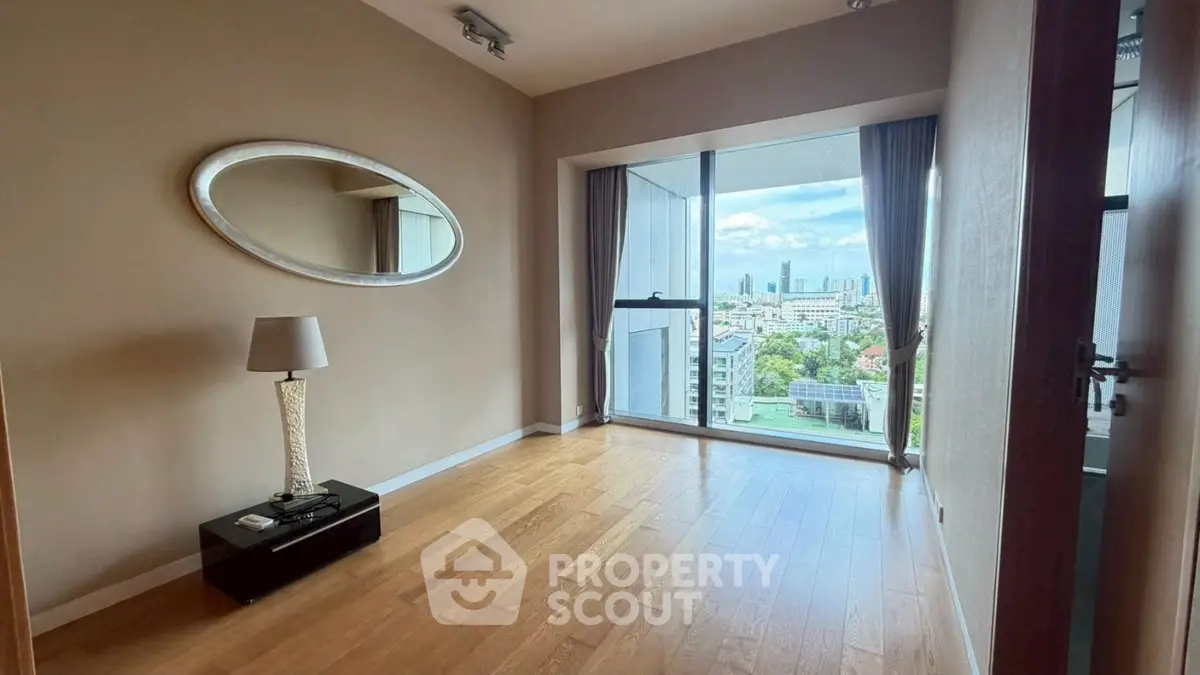 Spacious room with wooden flooring and large window offering stunning city views.