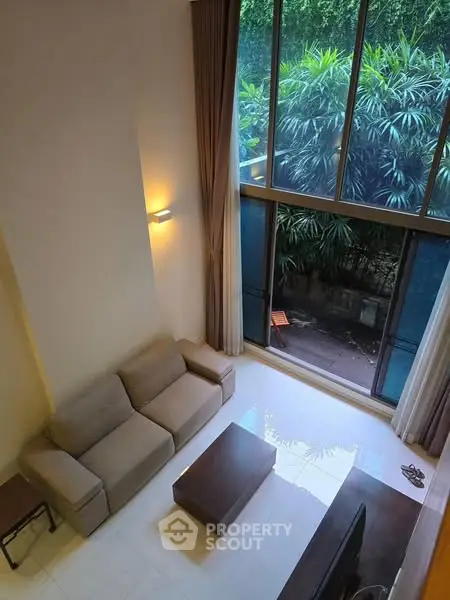Spacious living room with high ceiling and large windows overlooking lush greenery.