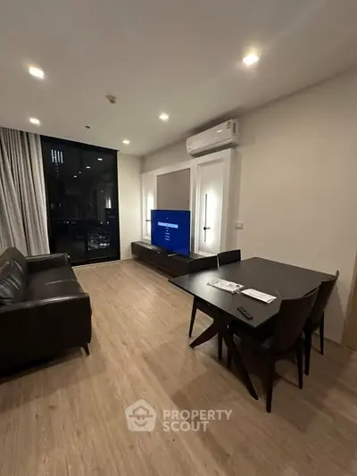 Modern living room with sleek furniture and large window offering city views.