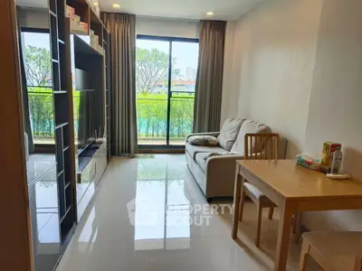 Modern living room with large window and cozy furniture overlooking greenery.