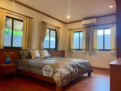 Spacious bedroom with wooden flooring and large windows for natural light.