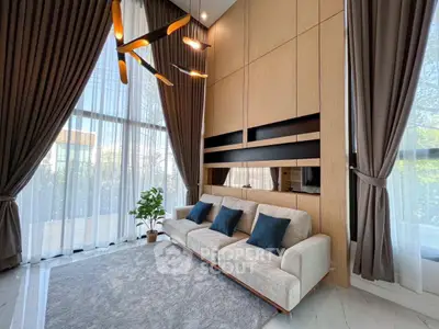 Luxurious living room with high ceilings, elegant curtains, and modern lighting.