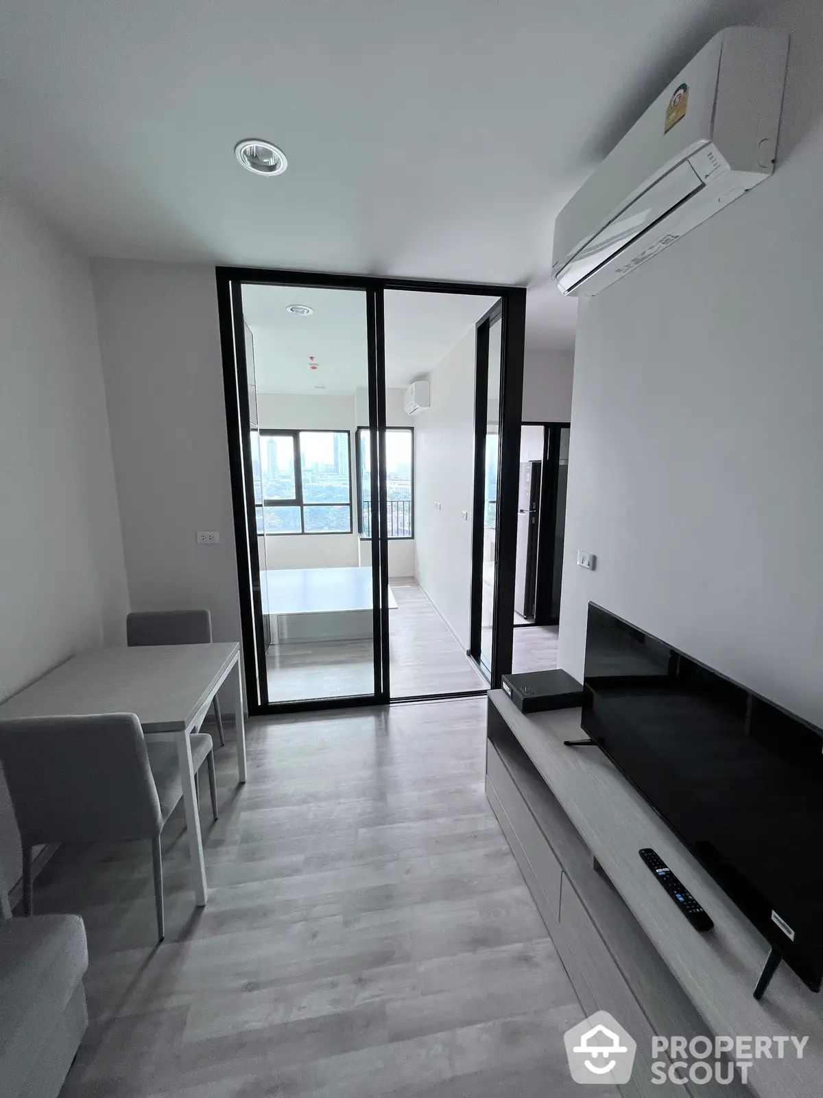 Sleek modern living room with glossy marble flooring, leading to a sunlit balcony through large glass doors, featuring minimalist furniture and a wall-mounted TV.