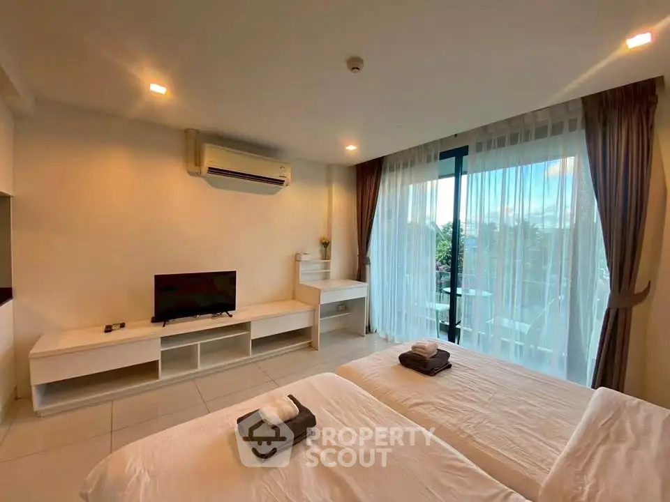 Spacious bedroom with twin beds, modern decor, and large window offering natural light.